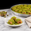 Koçak Bülbül Yuvası baklava: three nest-shaped pieces topped with crushed Antep pistachio on a white plate, with the full tray behind