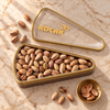Koçak triangle tin of roasted Antep pistachios, opened, with the clear KOÇAK lid beside it on a cream marble table
