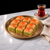 Koçak pistachio baklava: nine square pieces with a thick green Antep pistachio layer on a brass tray, served with Turkish tea