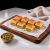 Koçak dry baklava: seven square pieces with a thin Antep pistachio layer on a wooden board