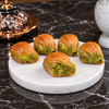 Koçak mussel baklava: five shell-shaped pieces of golden phyllo with a green Antep pistachio filling on a white marble board, one opened to show the filling